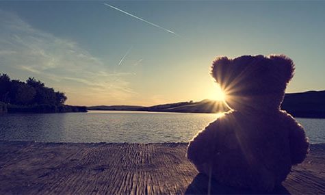 Vintage look of a teddy bear standing on wooden pier and looking at the sunset over lake. Concept for childhood memories childhood memories